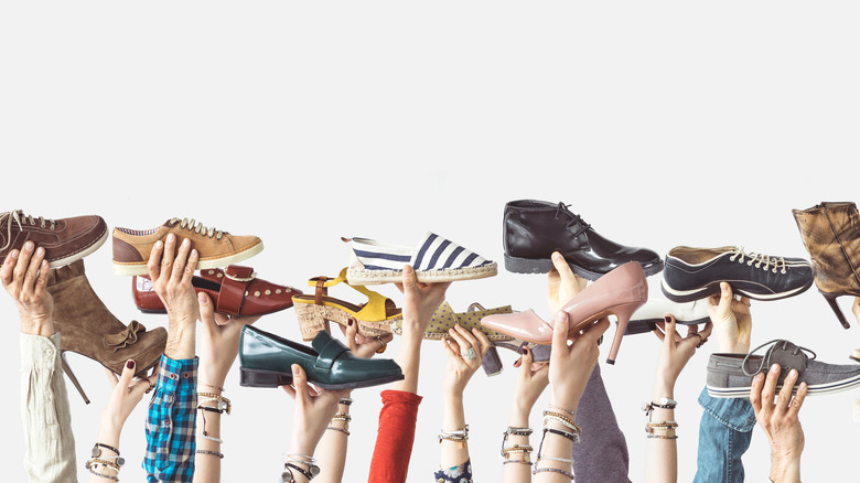 Many hands holding up different types of shoes 