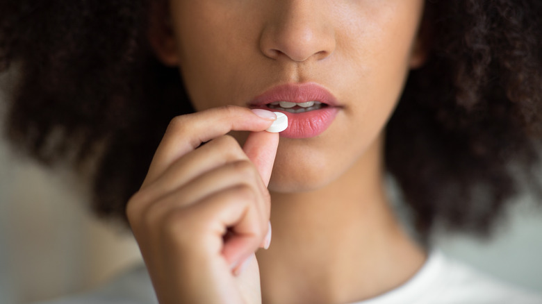 Woman holding white pill to mouth