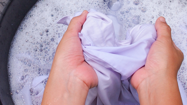 Hands scrubbing clothes in water basin