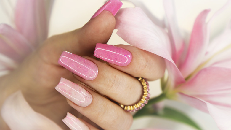 Pink false nails beside a pink Lily 