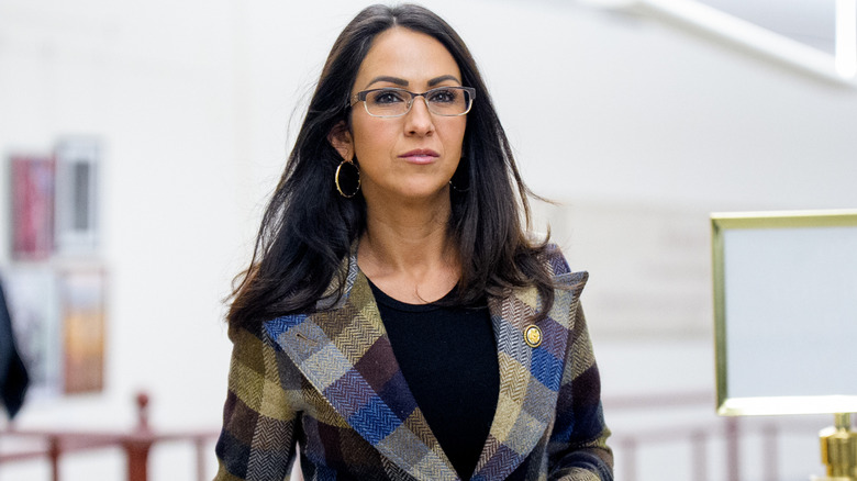Lauren Boebert grimacing while walking in a check blazer with a black top underneath it and glasses