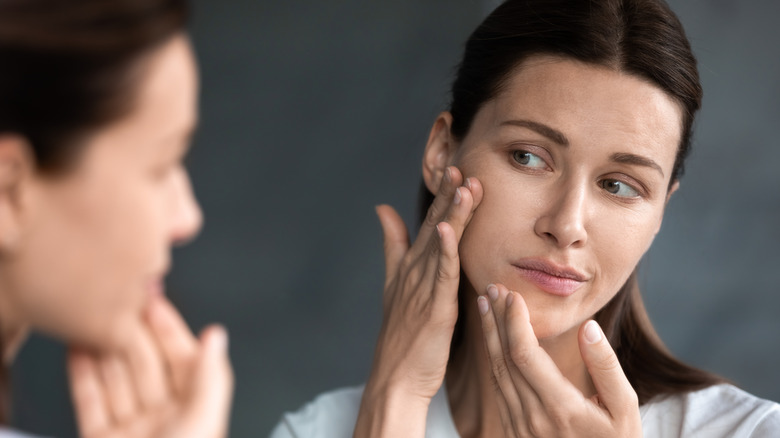 Woman looks at her dry skin in the mirror 