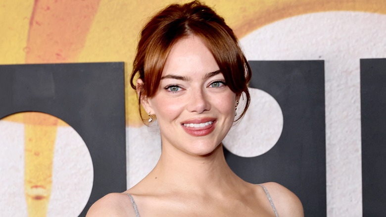 Emma Stone smiling with her tongue slightly out on the red carpet of a movie premiere