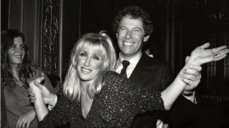 Alan Hamel smiling behind Suzanne Somers who's shrugging while her husband holds onto her.