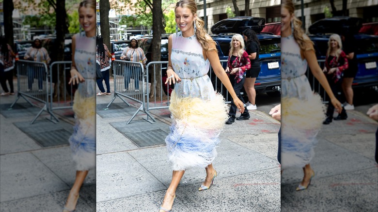Blake Lively on the sidewalk in New York, smiling and wearing a dress with a boa-feather skirt that's floating around her legs