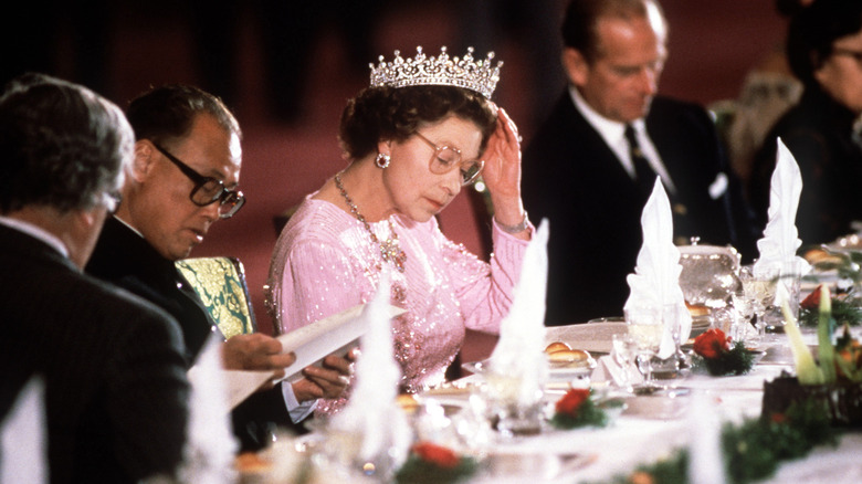 Queen Elizabeth II perusing a menu as she sits at a dining table with multiple people