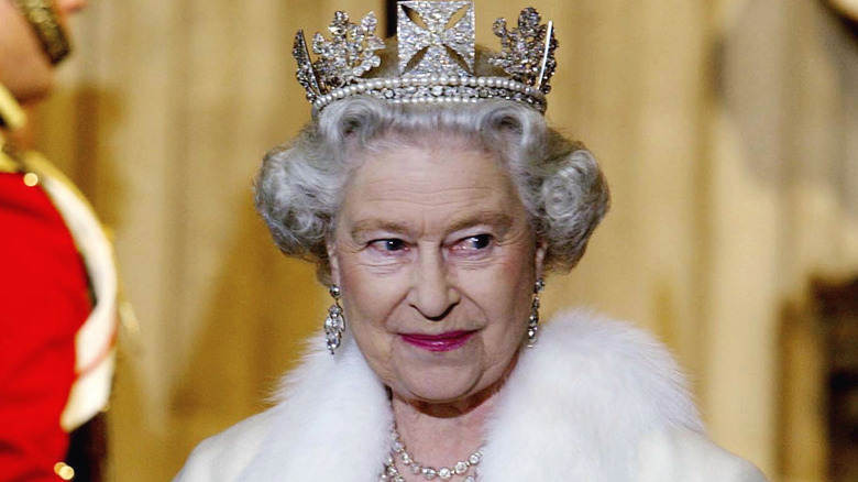 Queen Elizabeth II smiling in a crown, sparkly jewels, and a white fur-trimmed coat