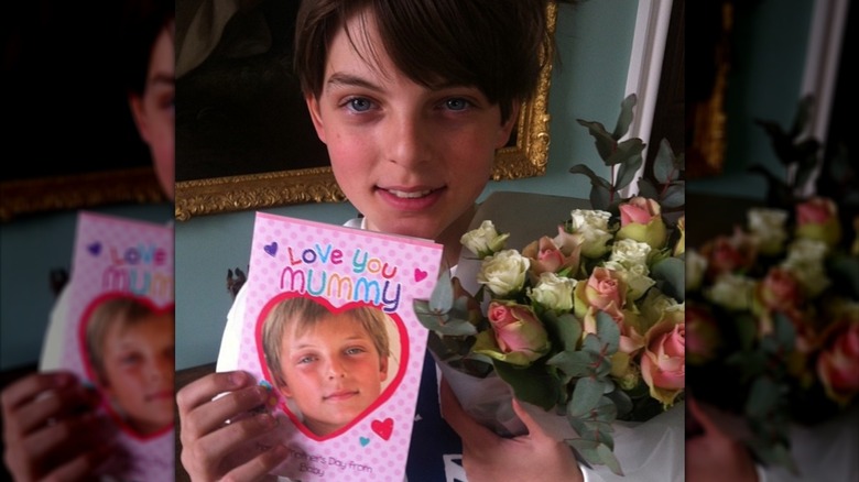 Damian Hurley holding a Mother's Day card and a bouquet.
