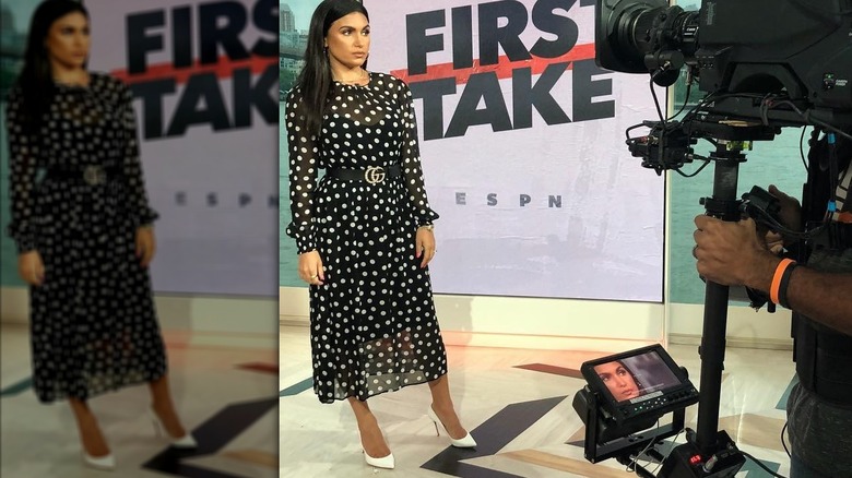Molly Qerim wearing a black and white polka dot dress with a camera pointed at her on set.
