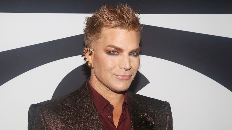 Adam Lambert smiling in a shimmering suit jacket with copper spikey hair