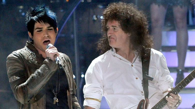 Adam Lambert singing into mic onstage next to Brian May playing guitar