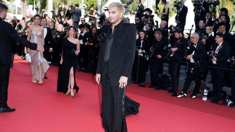 Adam Lambert posing on red carpet in Cannes, surrounded by photographers