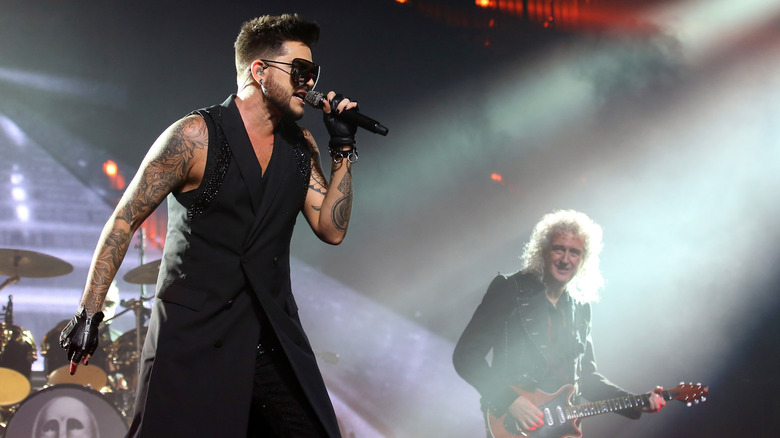 Adam Lambert singing into mic onstage next to Brian May playing guitar