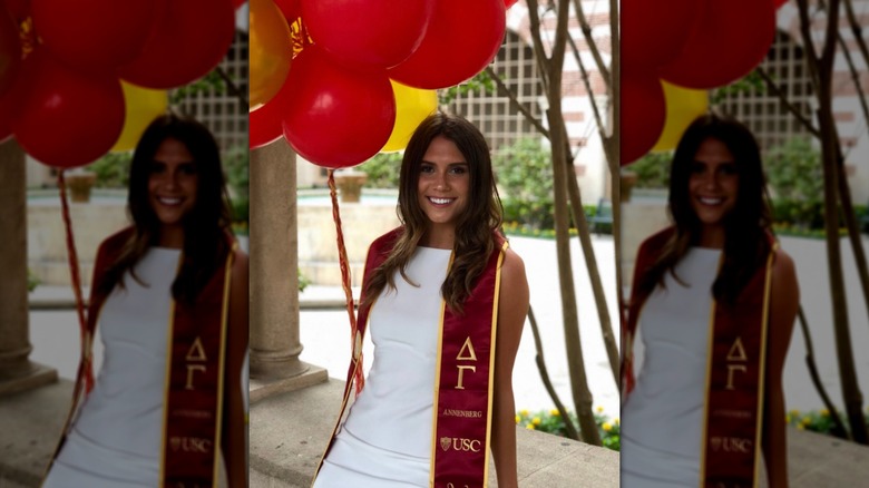 Sophie Flay smiles on her graduation day wearing red and gold USC colors in front of balloons.