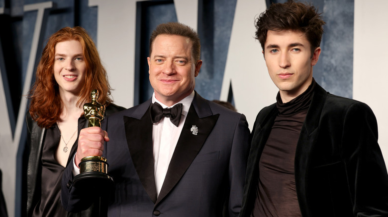 Brendan Fraser holds an award for his performance in "The Whale" next to his two sons wearing suits