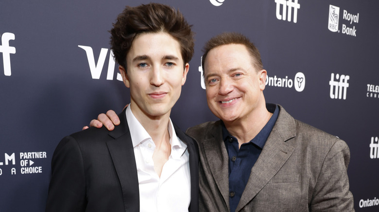 Brendan Fraser stands with his arm on his son Holden as they pose at a step and repeat