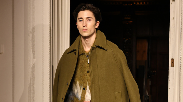 Brendan Fraser's son Holden has a serious face on the runway as he models a green jacket and sweater