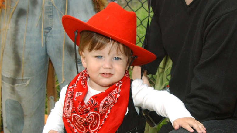 Holden Fraser  wears a red bandana and cowboy hat as a toddler outside