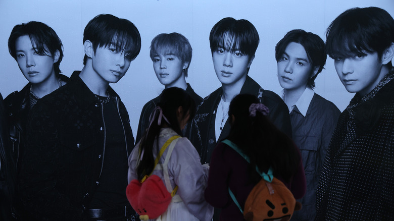 Two women in South Korea standing in front of a promo image of BTS.