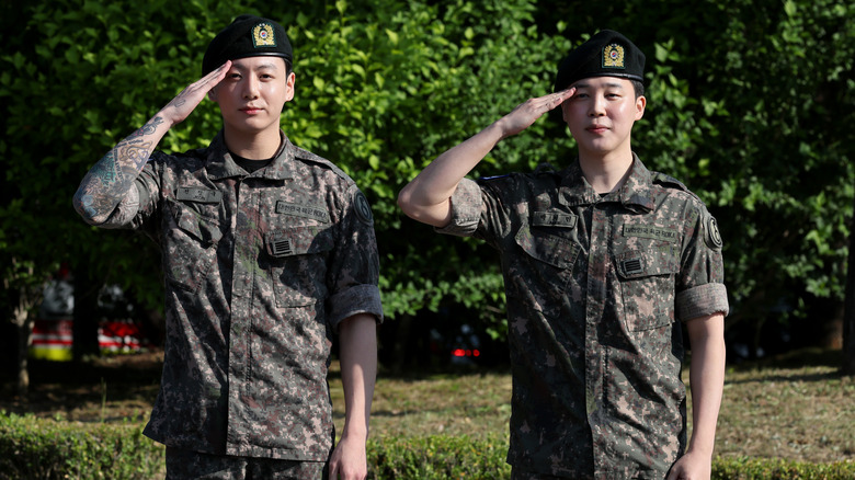Jungkook and Jimin saluting in their South Korean military uniforms in 2025.