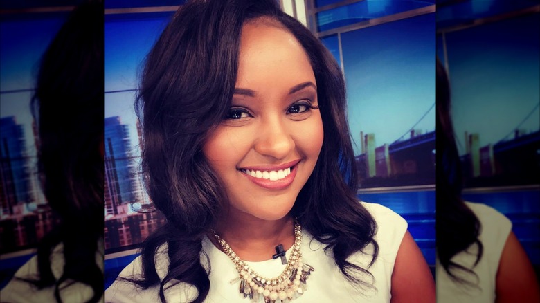 Rahel Solomon smiles on a newsroom set in a selfie showing off her curls wearing a white dress