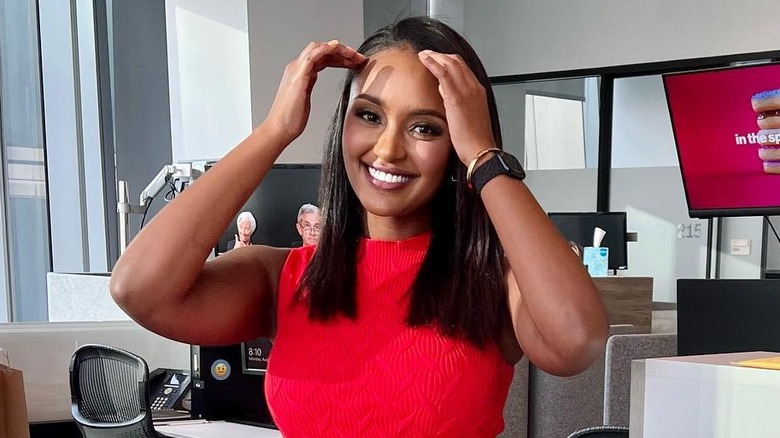 CNN's Rahel Solomon smiles in an office with her hands on her head wearing a red shirt