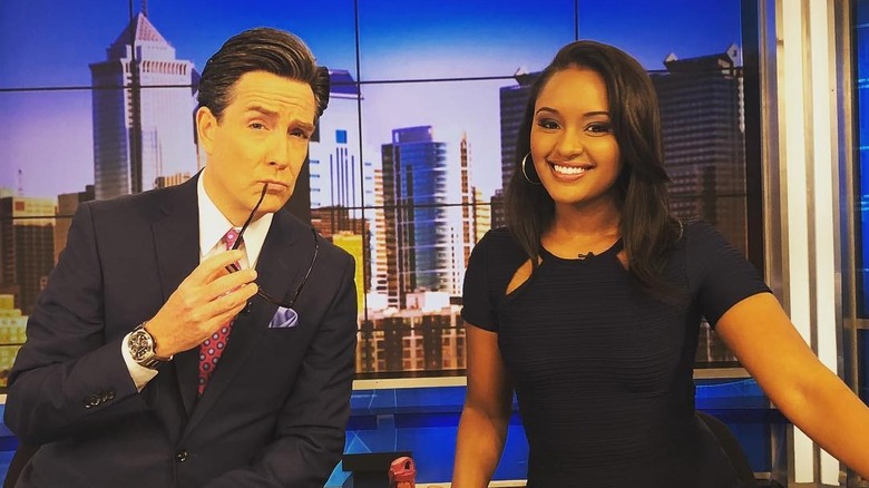 Rahel Solomon and her co-anchor Jim Donovan pose sitting at a newsdesk