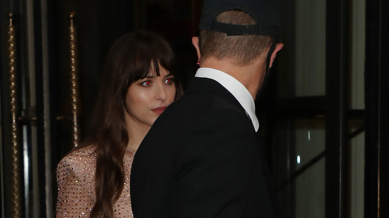 Chris Martin looking back at Dakota Johnson as they exit building