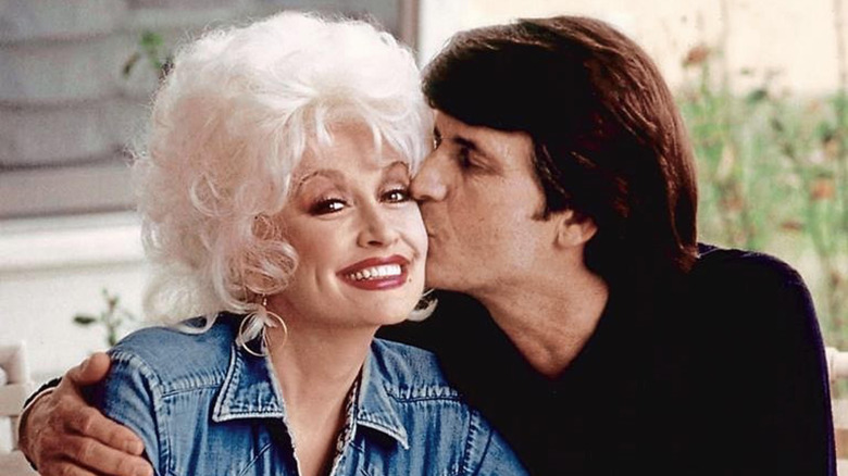 Dolly Parton smiles while Carl Dean kisses her on the cheek