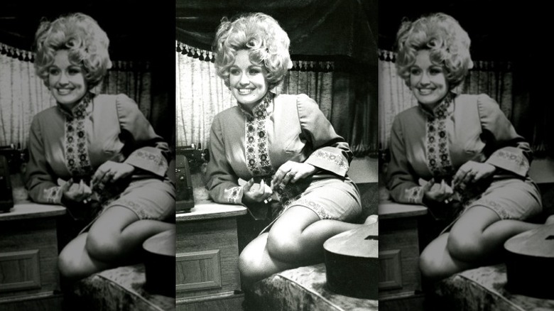 Young Dolly Parton posing on couch with guitar