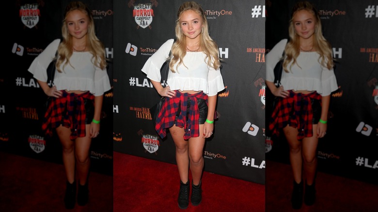 Natalie Alyn Lind wearing a plaid shirt tied around her waist with a white crop top and black shorts.