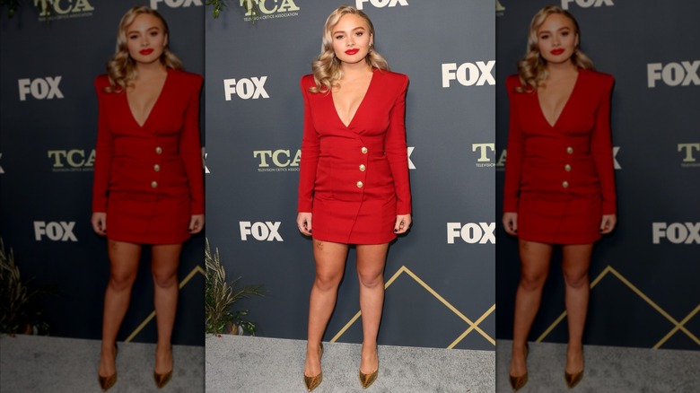 Natalie Alyn Lind posing in a short red suit dress.