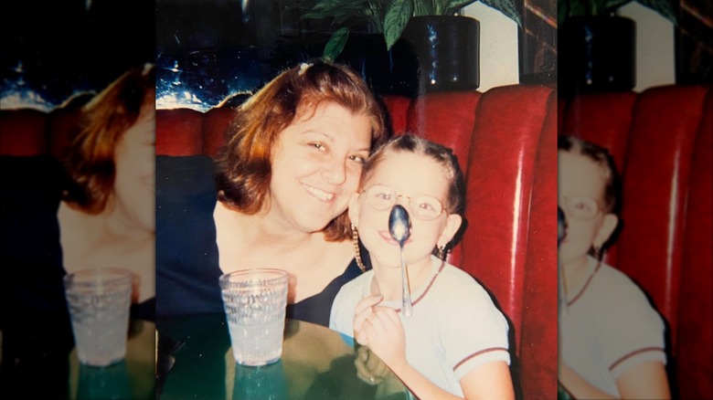 Young Eden Sher holding a spoon next to her mom in a booth