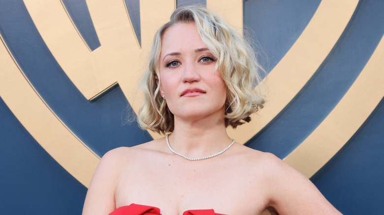 Emily Osment wearing a red dress while posing in front of the Warner Bros logo