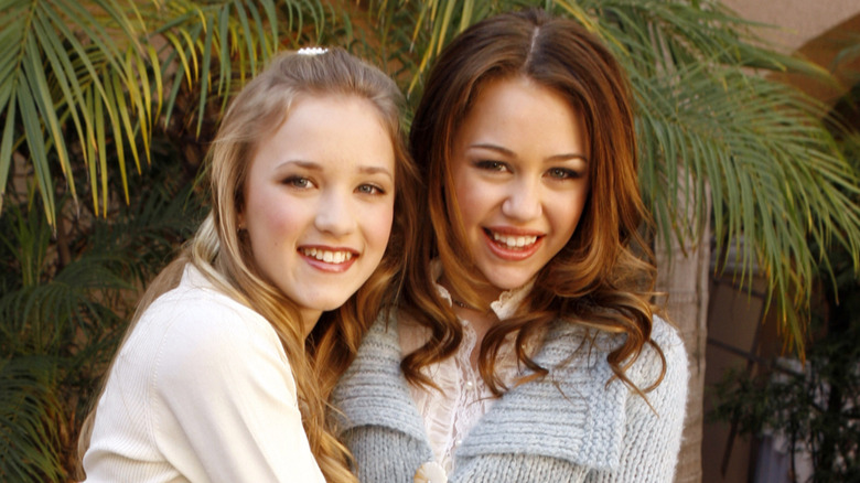 Young Emily Osment and Miley Cyrus smiling and embracing