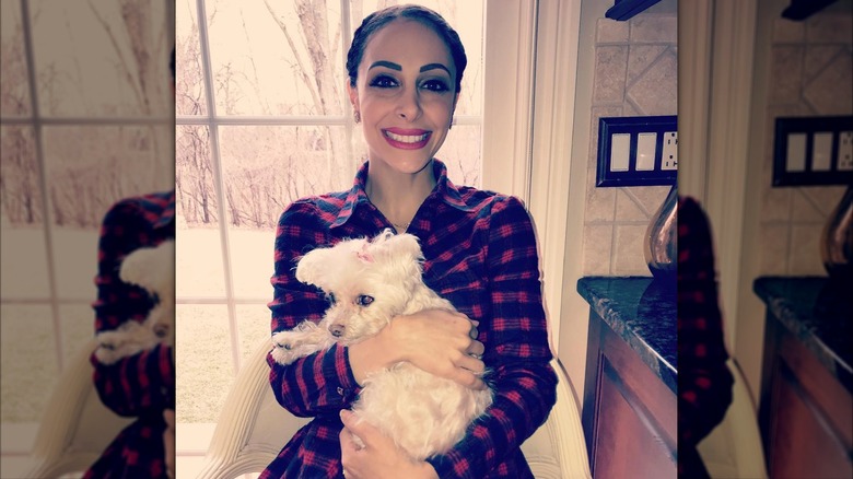 Deanna Stellato-Dudek wearing plaid pajamas and holding a fluffy white dog