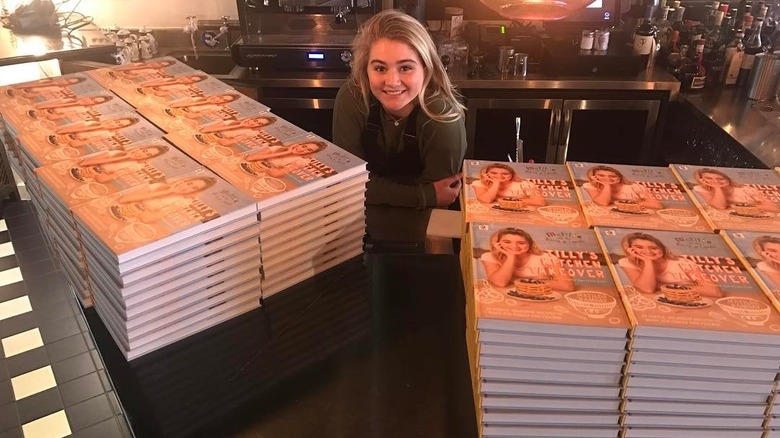 Tilly Ramsay smiling next to copies of her book