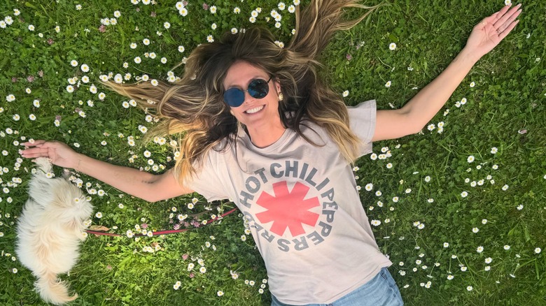 Heidi Klum laying on a grassy field with her arms outstretched and dog by her side in 2026