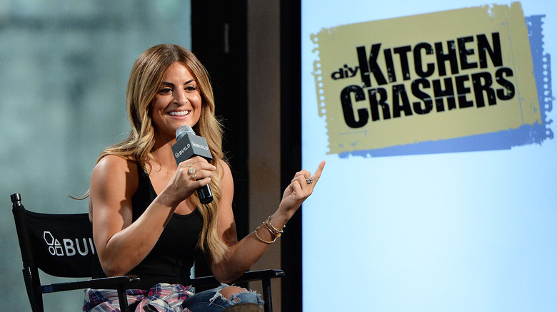 Alison Victoria speaking into a microphone in front of the Kitchen Crashers logo