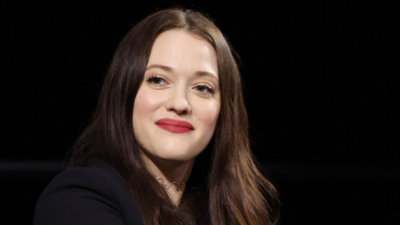 Kat Dennings smiling whole photographed in front of a black background