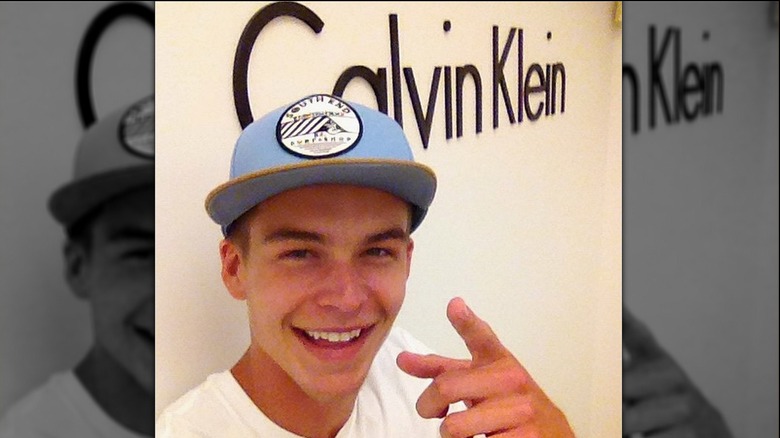 Mitchell Slaggert in blue ball cap smiling and pointing to Calvin Klein logo