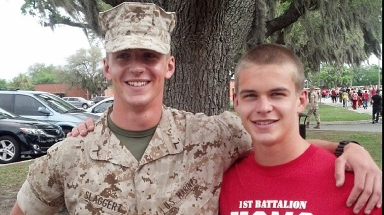 Mitchell Slaggert in red shirt with buzzed hair standing with arm around a Marine in uniform