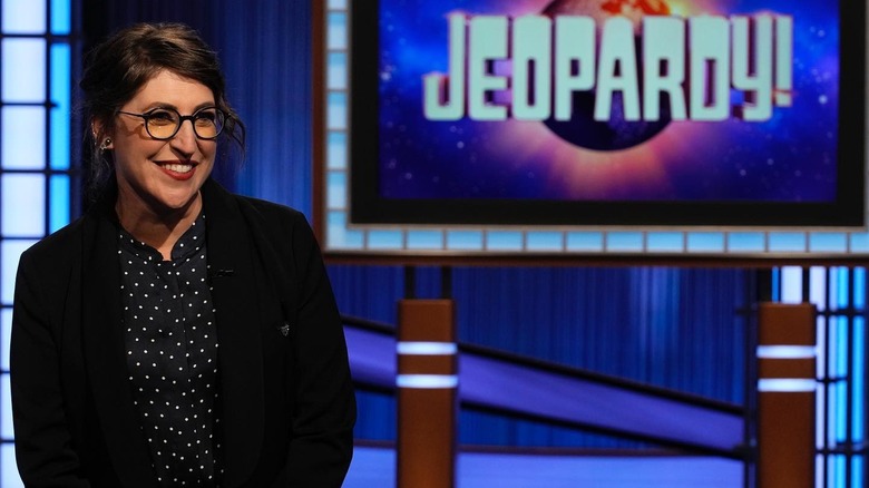Mayim Bialik posing in front of Jeopardy! logo