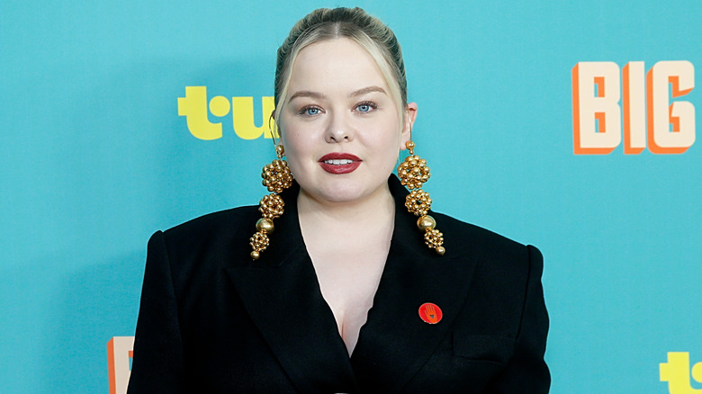 Nicola Coughlan in black blazer with big gold earrings and red lapel pin
