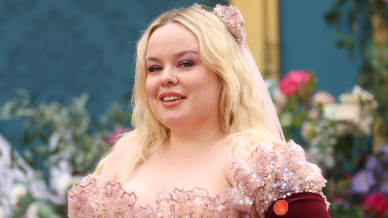Nicola Coughlan in pink beaded gown with pink bow in hair standing in front of flowers