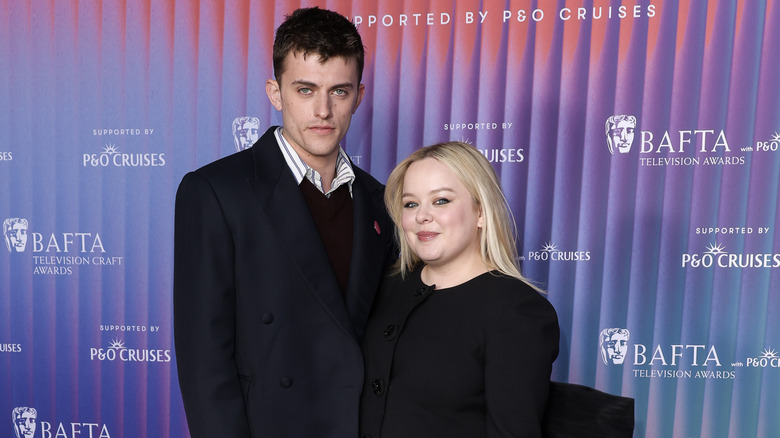 Nicola Coughlan in black dress with hair straight next to Jake Dunn in dark blazer and striped shirt