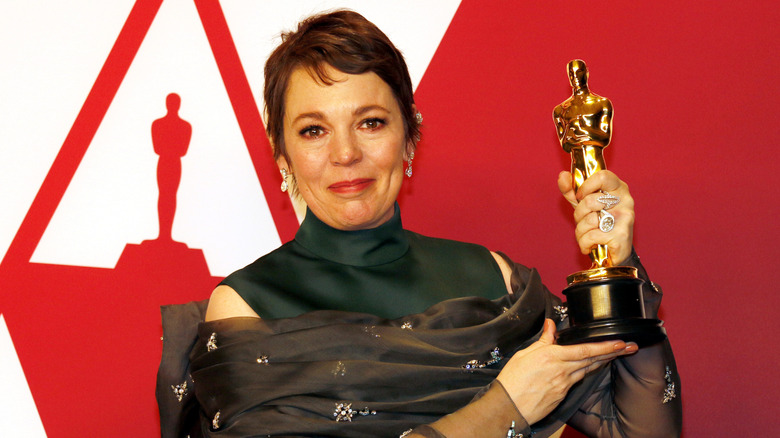 Actor Olivia Colman holds up her Oscar award in a black turtleneck dress in 2019