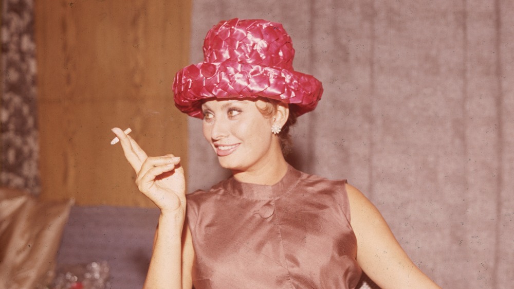 Sophia Loren smoking a cigarette, wearing a red hat