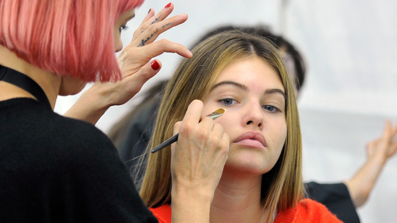 Makeup artist holding a brush as she paints Thylane Blondeau's face in 2017