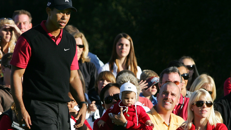 A baby Sam Woods in the audience of golf game with her mother as Tiger Woods walks past